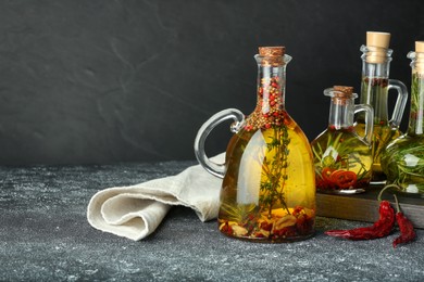Photo of Cooking oil with different spices and herbs in jugs on light grey table. Space for text