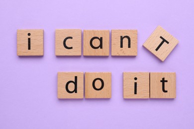 Motivation concept. Changing phrase from I Can't Do It into I Can Do It by removing wooden square with letter T on violet background, top view