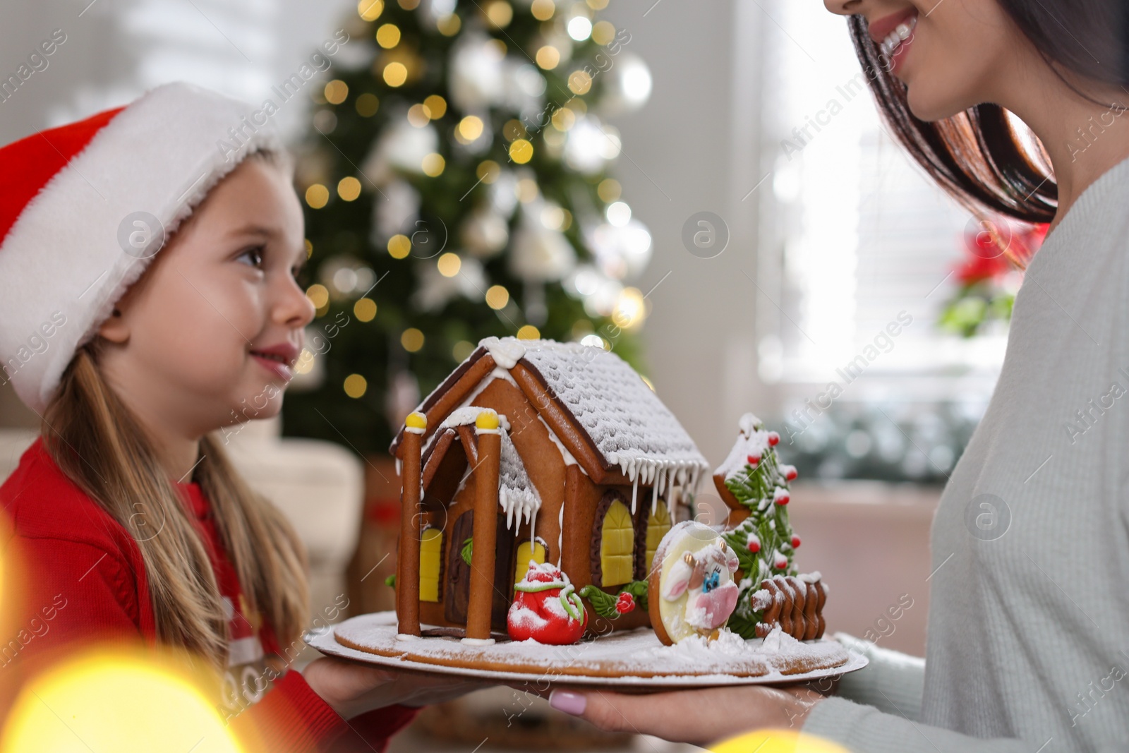 Photo of Mother and daughter with gingerbread house indoors, closeup