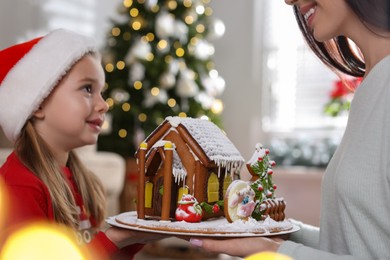 Mother and daughter with gingerbread house indoors, closeup