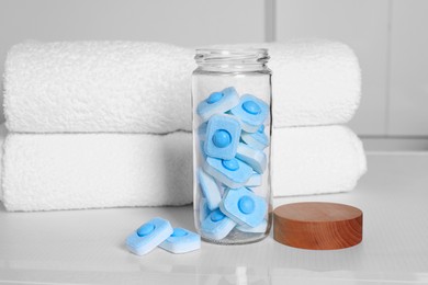 Photo of Glass jar with water softener tablets on washing machine in bathroom