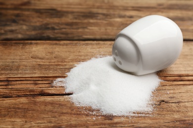 Scattered salt and shaker on wooden table, closeup