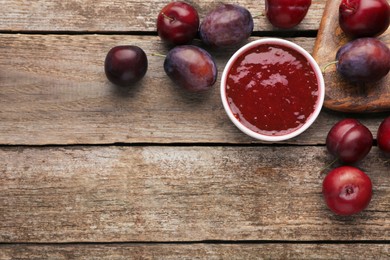Photo of Plum puree in bowl and fresh fruits on wooden table, flat lay. Space for text