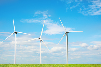 Image of Alternative energy source. Wind turbines in field under blue sky