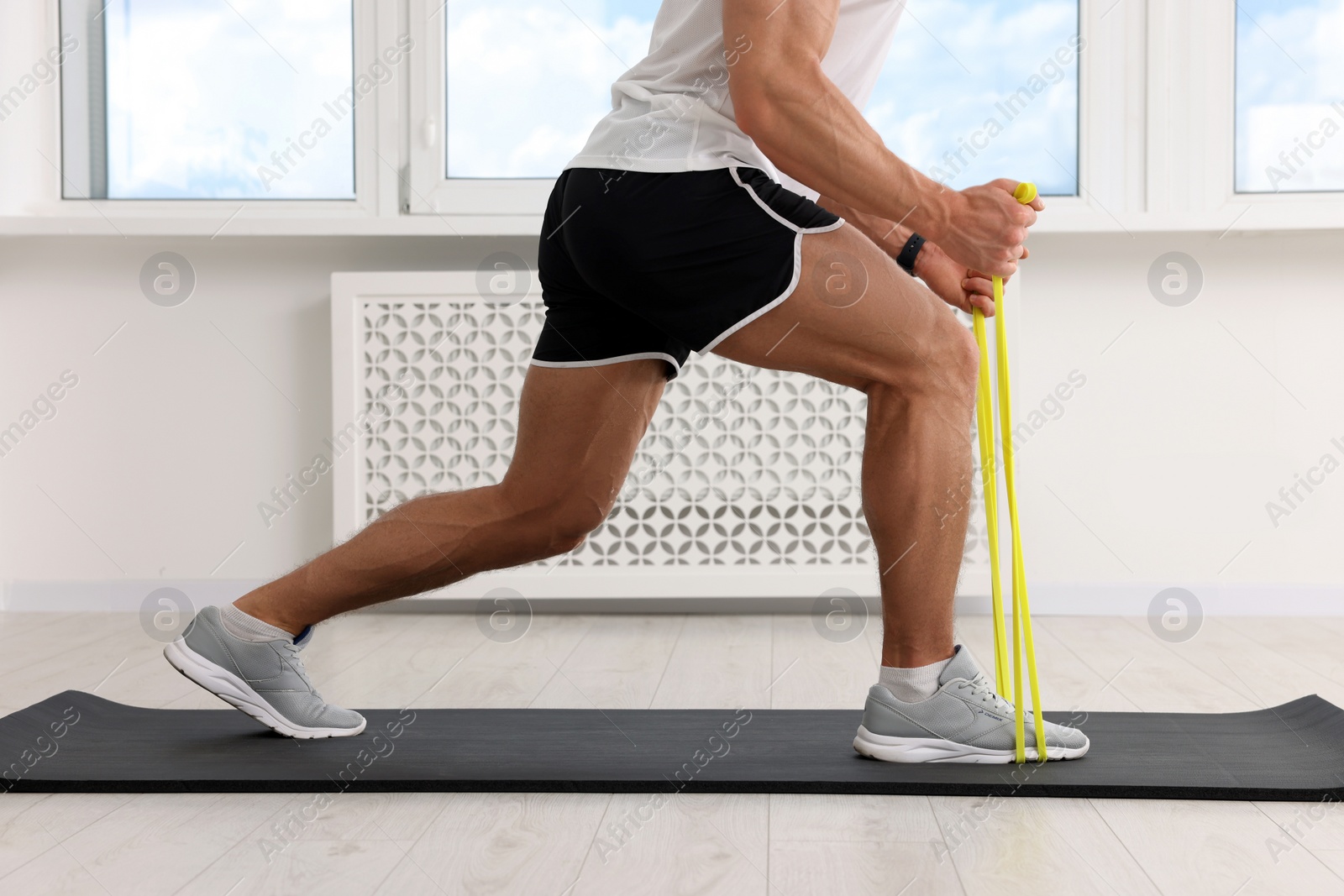 Photo of Athletic man doing exercise with elastic resistance band on mat indoors, closeup