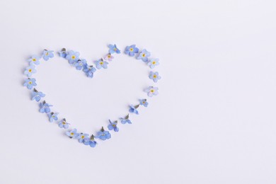 Heart made with beautiful forget-me-not flowers on white background, top view. Space for text