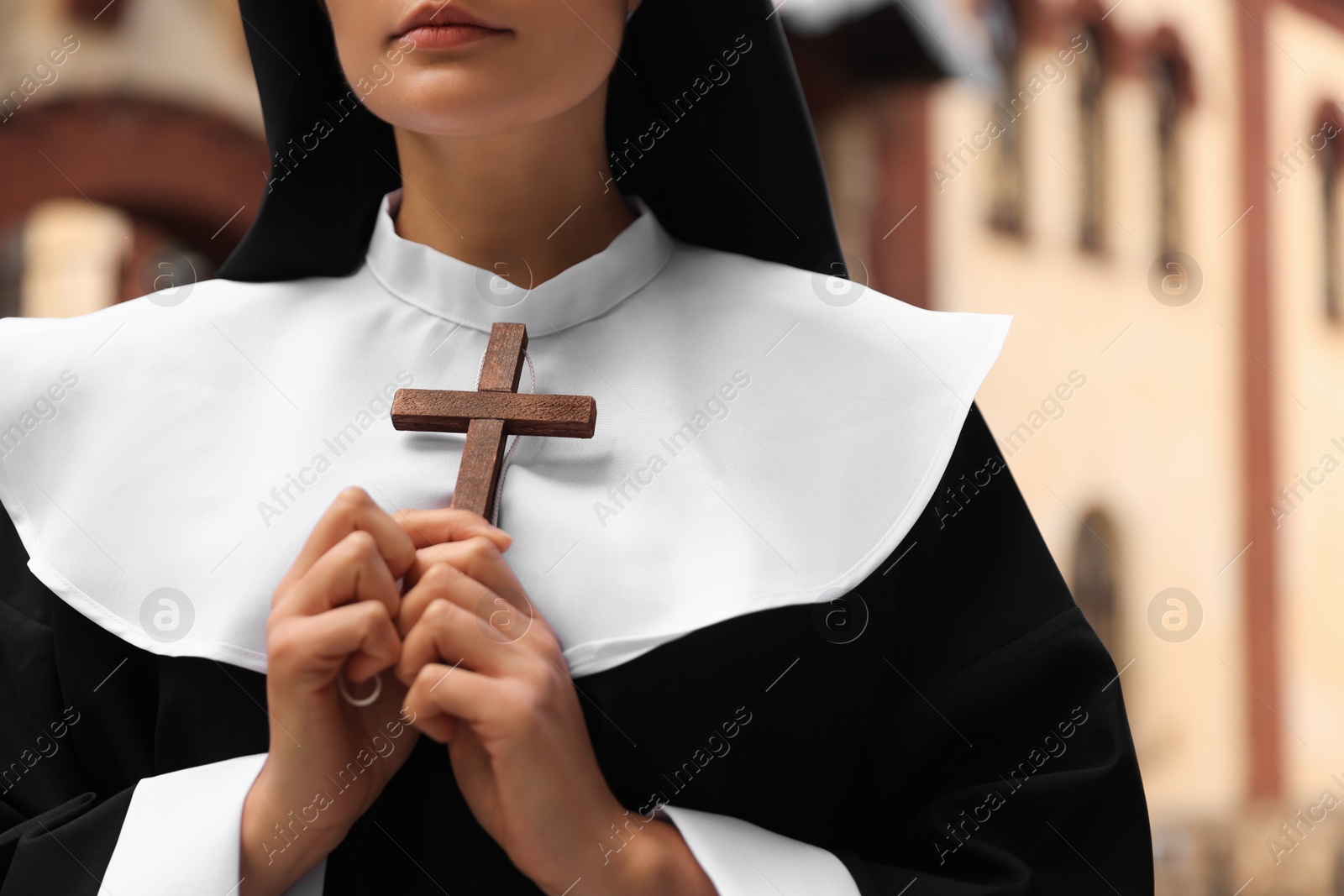 Photo of Young nun holding Christian cross near building outdoors, closeup