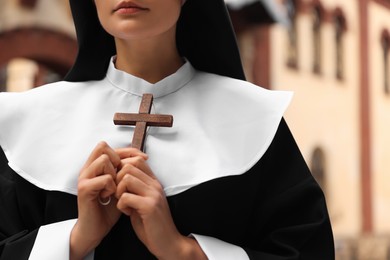 Young nun holding Christian cross near building outdoors, closeup