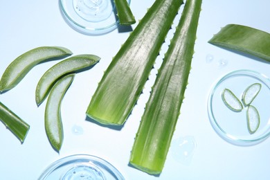 Cut aloe vera and cosmetic gel on light blue background, flat lay