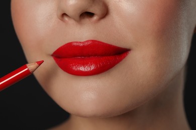 Photo of Young woman with beautiful red lip pencil on black background, closeup