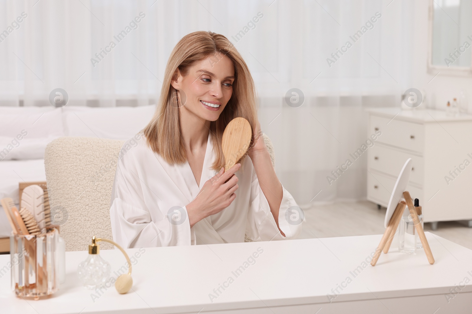 Photo of Beautiful woman brushing her hair at vanity in bedroom