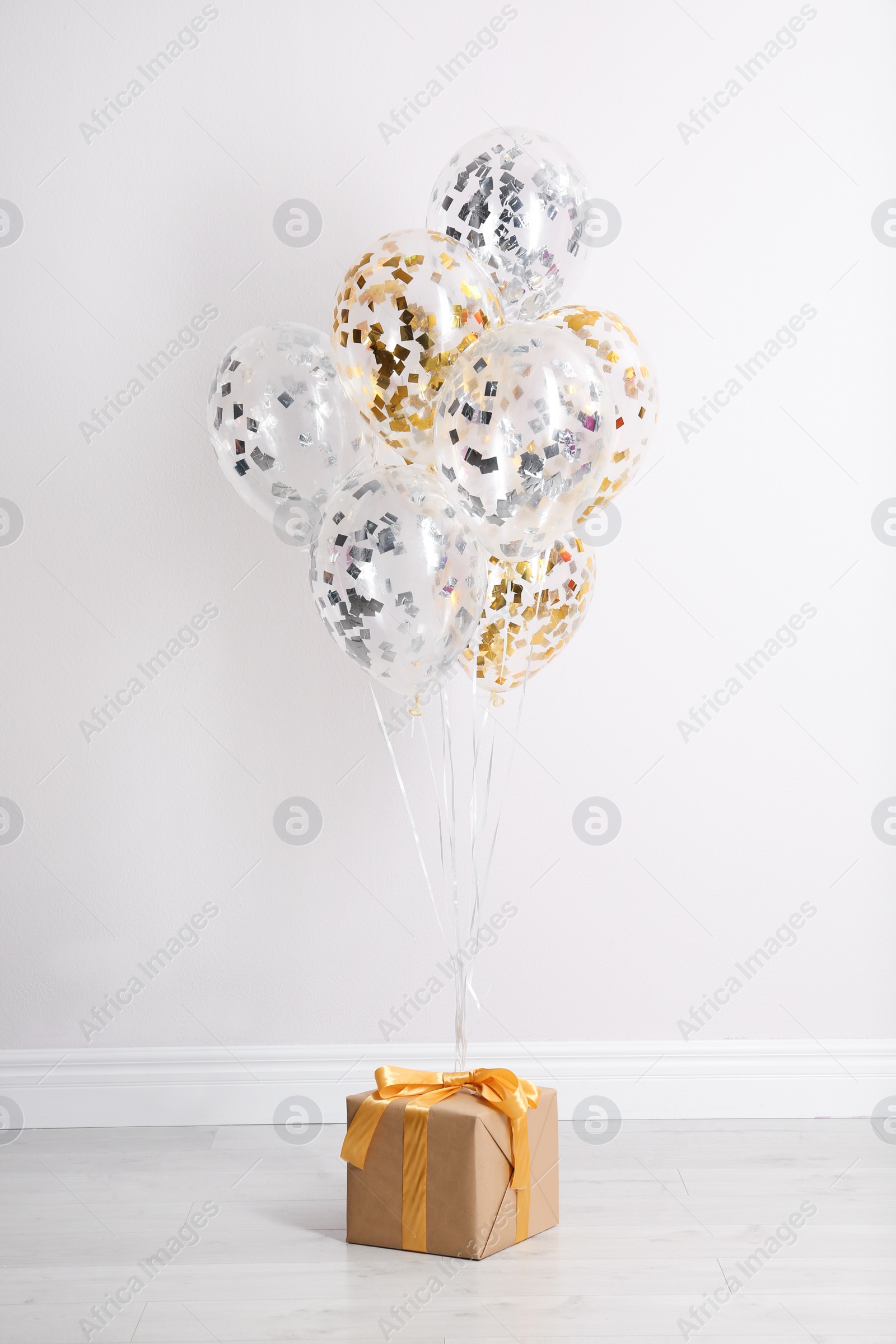 Photo of Bright balloons and gift box on floor against white wall