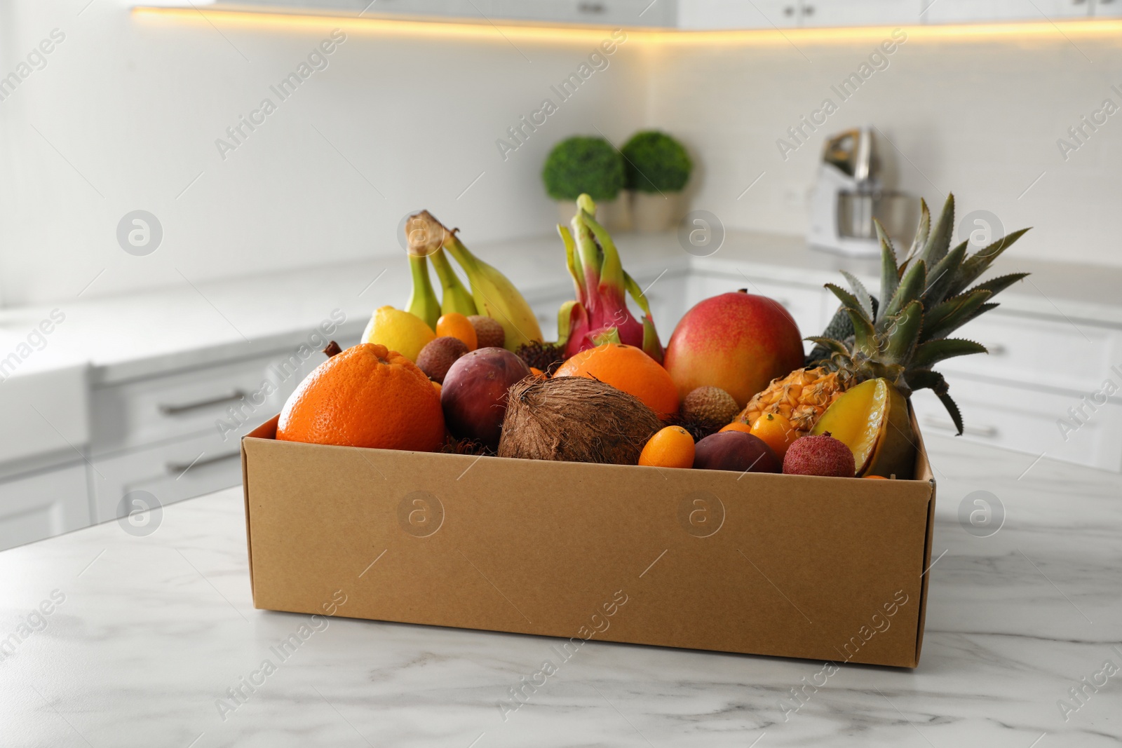 Photo of Cardboard box with assortment of exotic fruits on table in kitchen