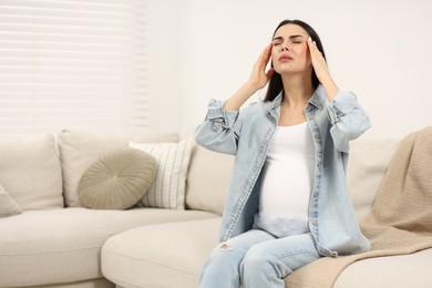 Pregnant woman suffering from headache on sofa at home, space for text