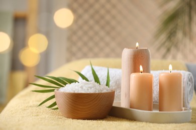 Photo of Spa composition. Burning candles, sea salt and towel on soft yellow surface