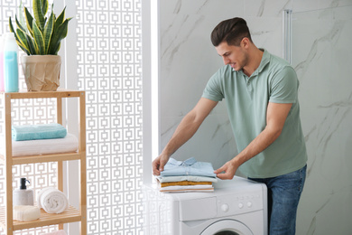 Happy man with clean clothes near washing machine in bathroom. Laundry day