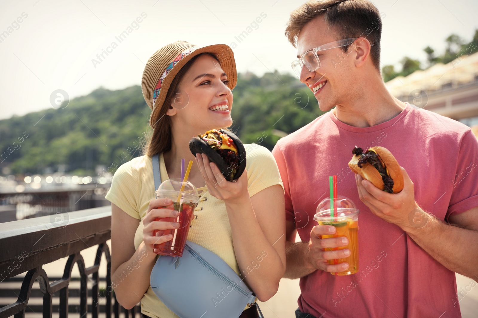 Photo of Young happy couple with burgers walking on city street