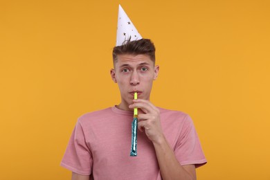 Photo of Young man in party hat with blower on orange background