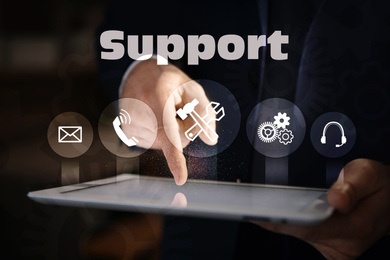 Image of Businessman using digital tablet and different icons on dark background, closeup. Technical support service 
