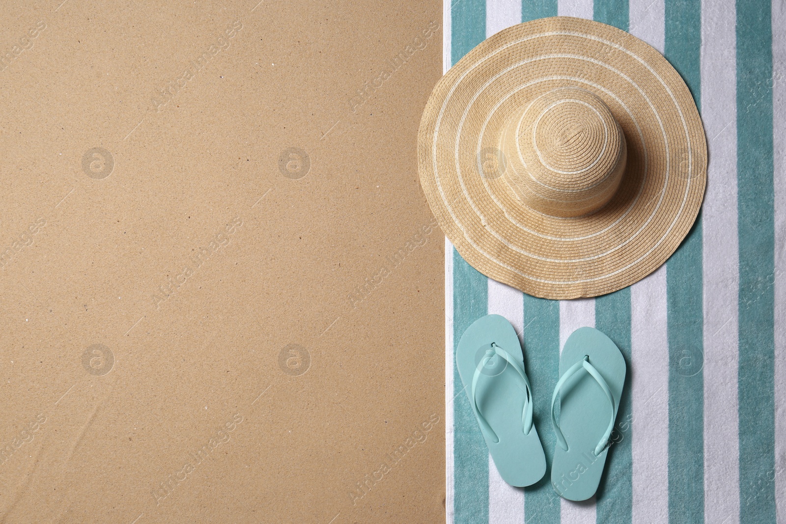 Photo of Straw hat, flip flops and space for text on beach sand, top view. Summer vacation