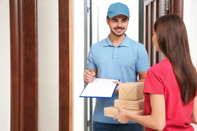 Photo of Woman receiving parcels from delivery service courier indoors
