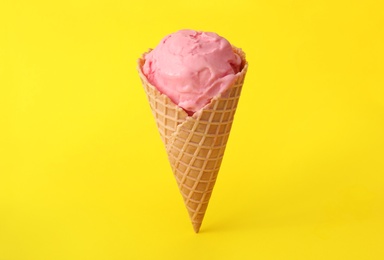 Photo of Delicious pink ice cream in waffle cone on yellow background