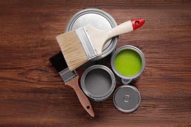 Cans of paints and brushes on wooden table, flat lay