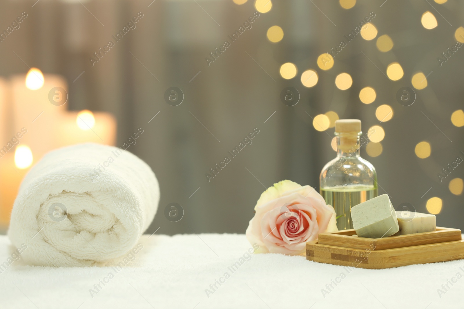 Photo of Beautiful composition with different spa products and rose on white towel against blurred lights