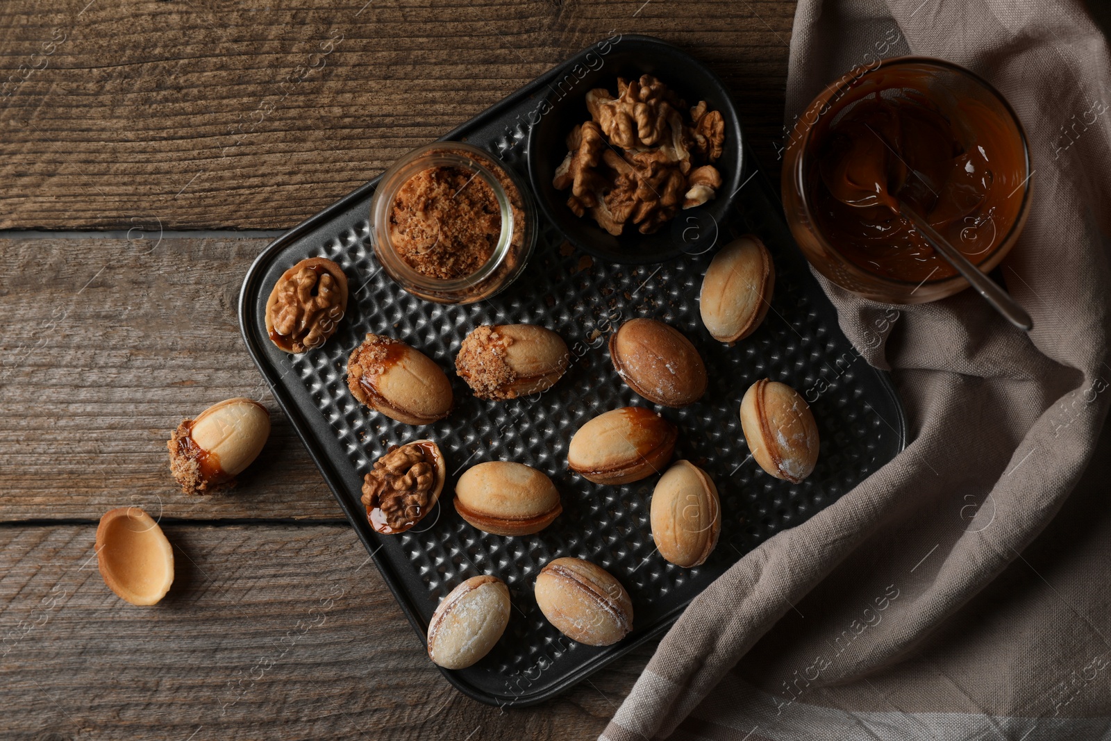 Photo of Freshly baked homemade walnut shaped cookies, boiled condensed milk and nuts on wooden table, flat lay