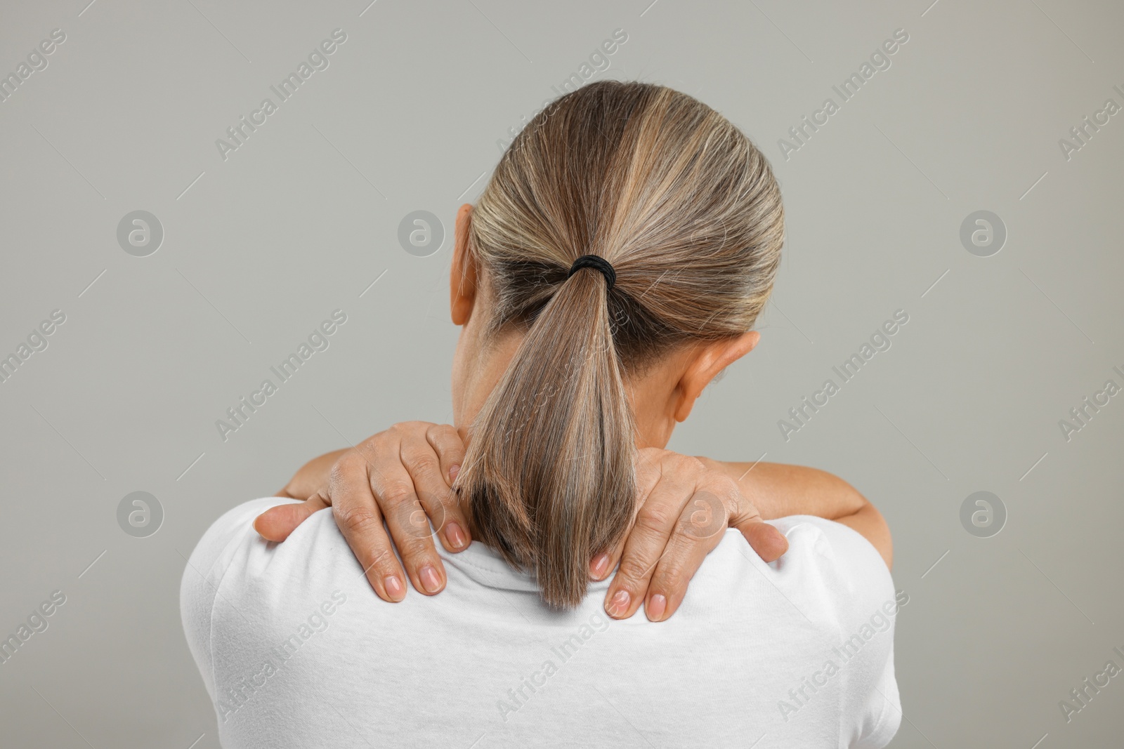 Photo of Mature woman suffering from pain in her neck on grey background, back view