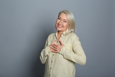 Happy woman holding hands near heart on grey background