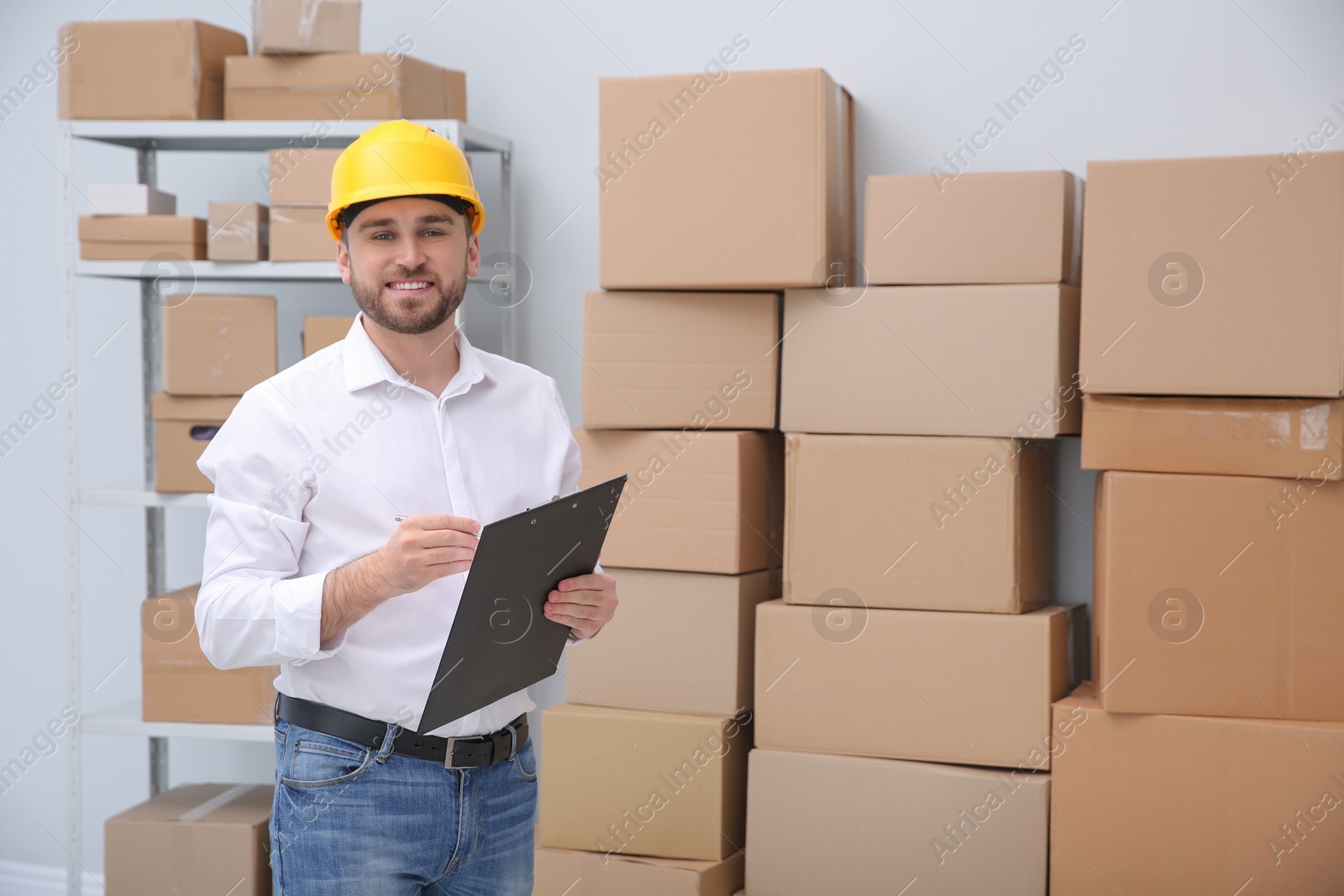 Photo of Young man with clipboard near cardboard boxes at warehouse