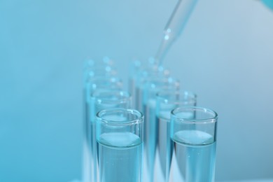 Laboratory analysis. Dripping reagent into test tube on light blue background, closeup