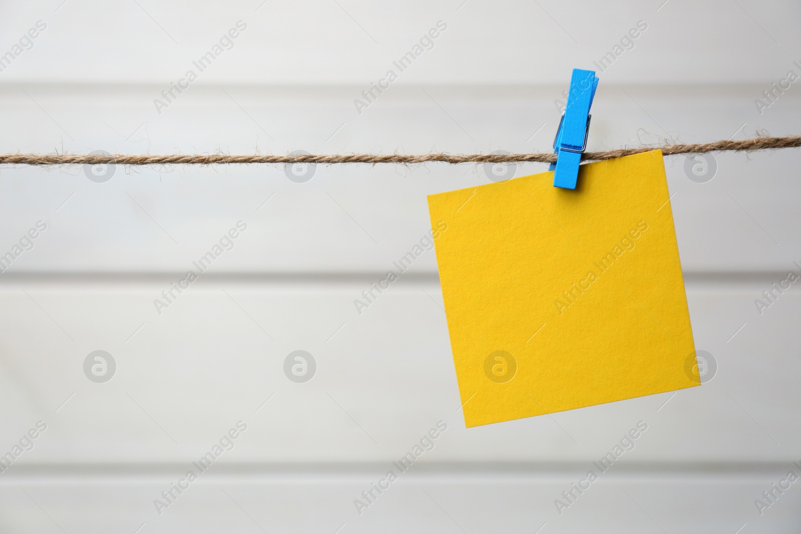 Photo of Clothespin with blank notepaper on twine against white wooden background. Space for text