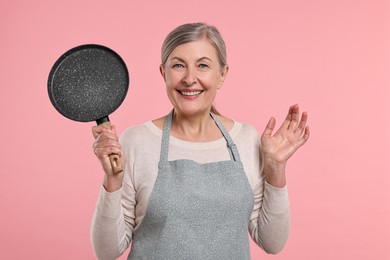 Photo of Happy housewife with frying pan on pink background