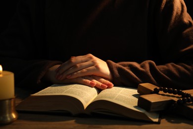 Woman praying at table with burning candle and Bible, closeup