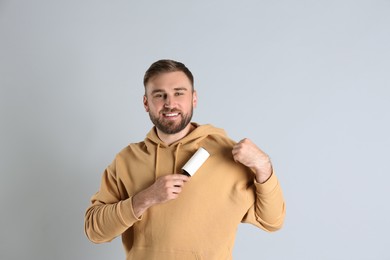 Young man cleaning clothes with lint roller on grey background