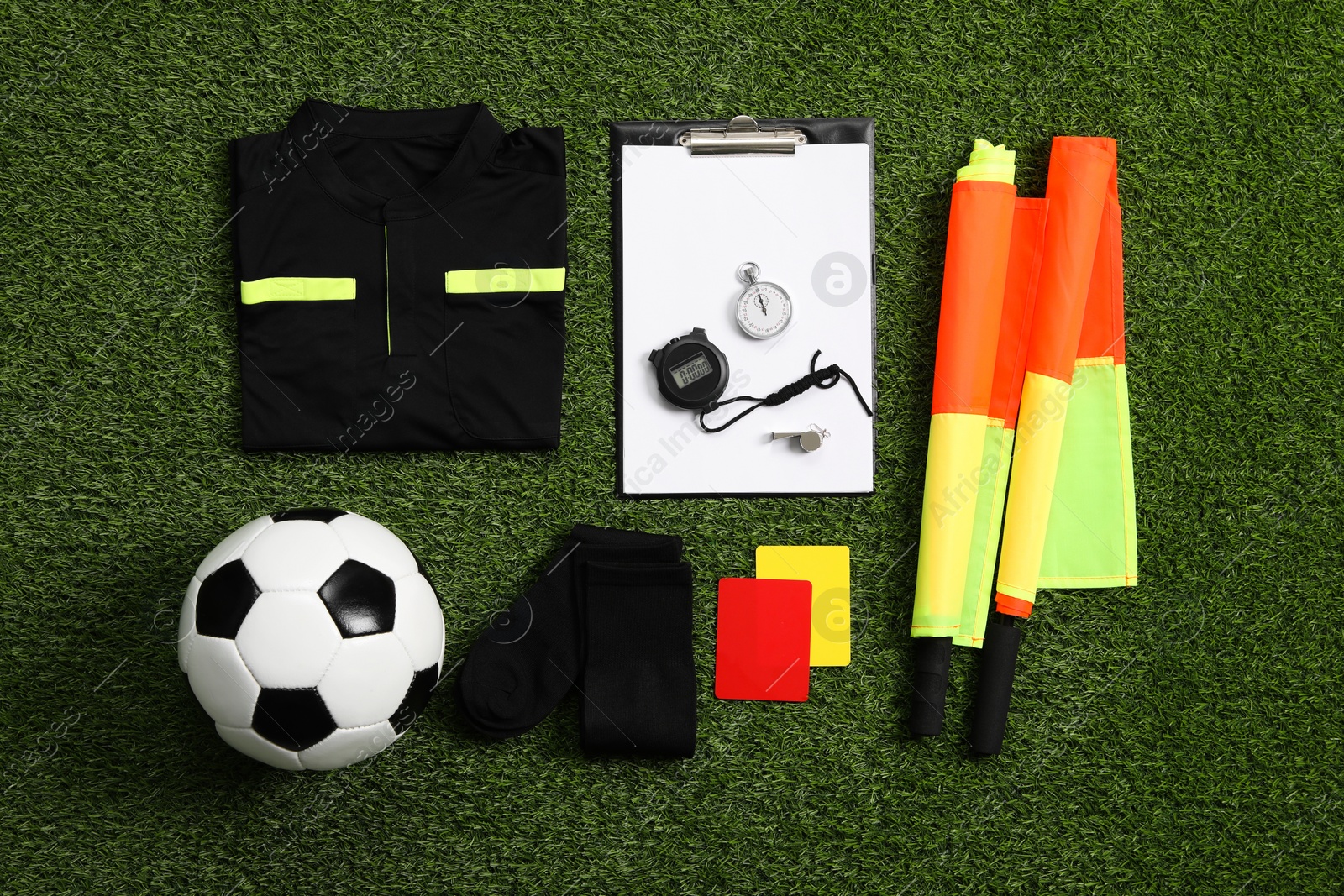 Photo of Uniform, soccer ball and other referee equipment on green grass, flat lay