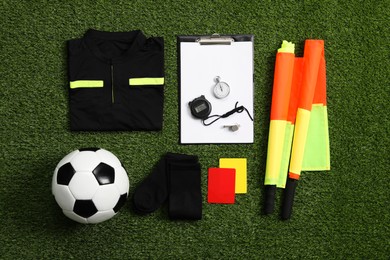 Uniform, soccer ball and other referee equipment on green grass, flat lay