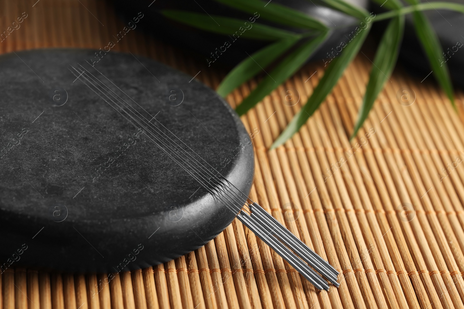 Photo of Acupuncture needles and spa stone on bamboo mat, closeup