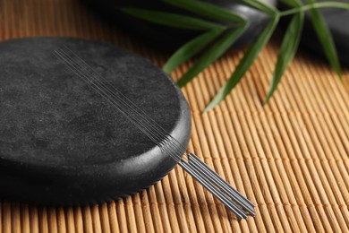 Photo of Acupuncture needles and spa stone on bamboo mat, closeup