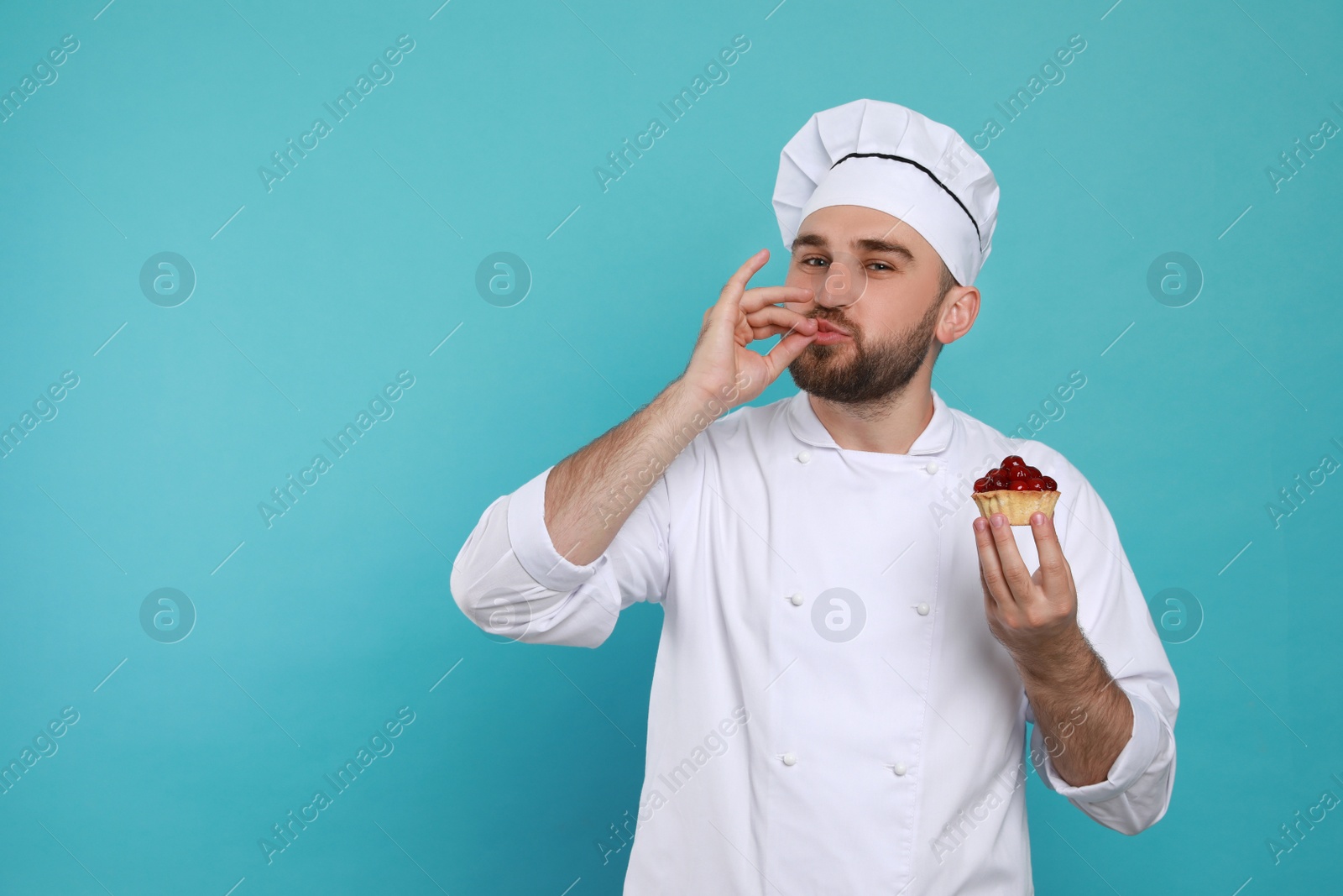 Photo of Happy professional confectioner in uniform with tartlet showing delicious gesture on light blue background. Space for text