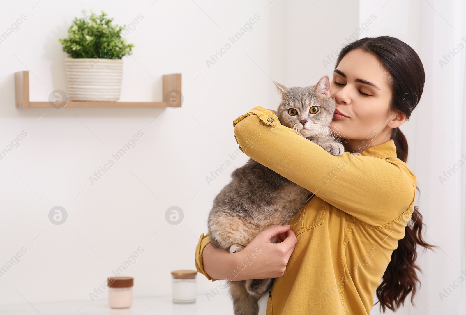 Photo of Young woman kissing her adorable cat at home, space for text