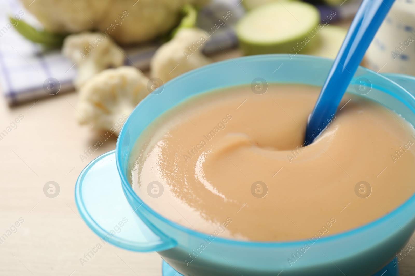 Photo of Spoon of healthy baby food over bowl on table, closeup