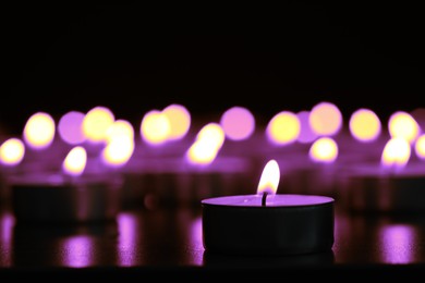 Burning violet candle on black background, closeup. Funeral attributes