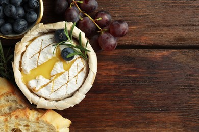 Photo of Tasty baked brie cheese and products on wooden table, flat lay. Space for text