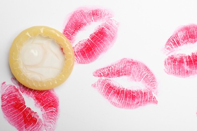 Condom and lipstick kiss marks on white background, top view. Safe sex