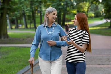 Senior lady with walking cane and young woman in park