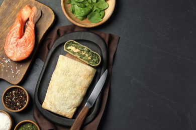 Flat lay composition of delicious strudel with salmon and spinach served on dark textured table. Space for text