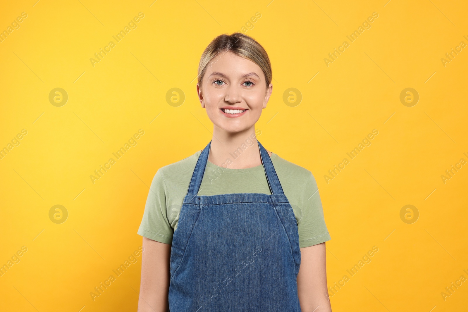 Photo of Beautiful young woman in denim apron on orange background